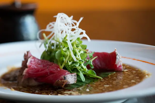 Seared tataki slices topped with scallions and shredded daikon in sauce