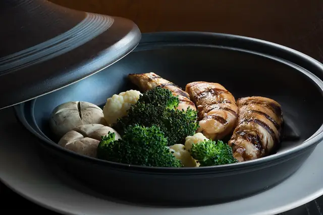 Dark lidded bowl with grill-marked pieces, broccoli, cauliflower and mushrooms