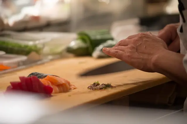 Chef’s hands slicing fish on a wooden cutting board