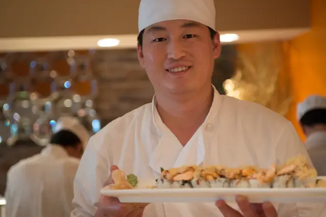 Sushi chef smiling while holding a platter of rolls