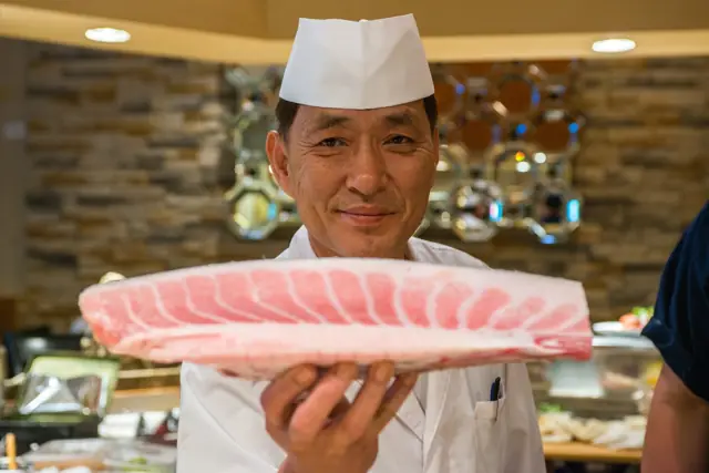 Smiling sushi chef holding up a fresh fish fillet