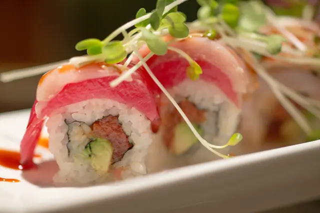 Close-up of a tuna-topped sushi roll garnished with microgreens