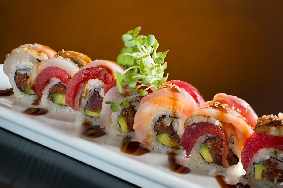 Colorful specialty roll topped with tuna and salmon on a long white plate