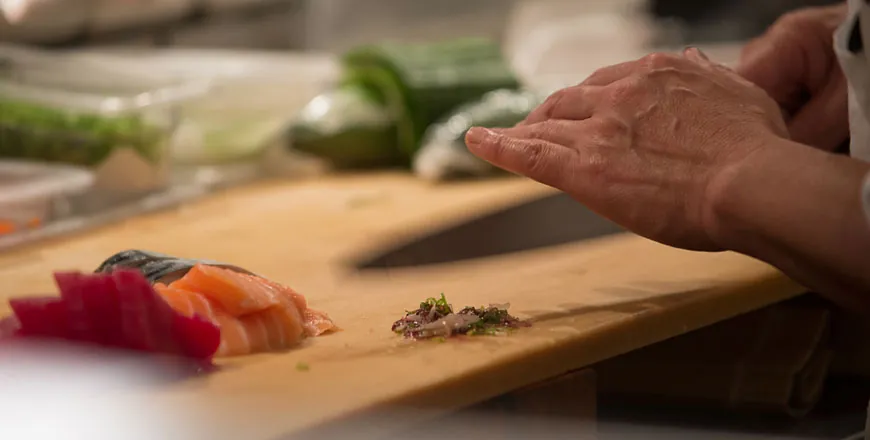 Close-up of hands slicing fresh fish on a wooden cutting board