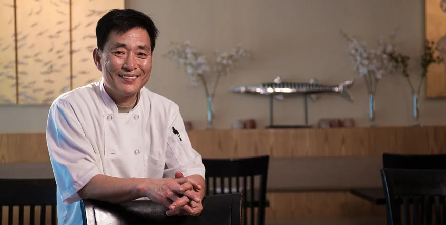 Chef Lee smiling in his white chef’s jacket in the dining room